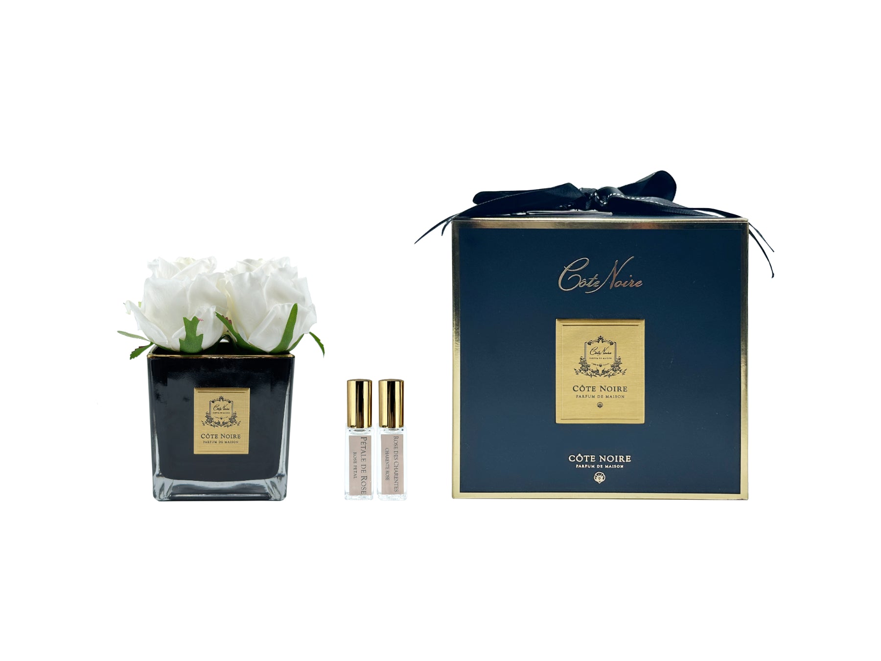 vier weisse rosen in schwarzer quadratischer vase neben zwei pafrumsprays und geschenkbox mit schleife.