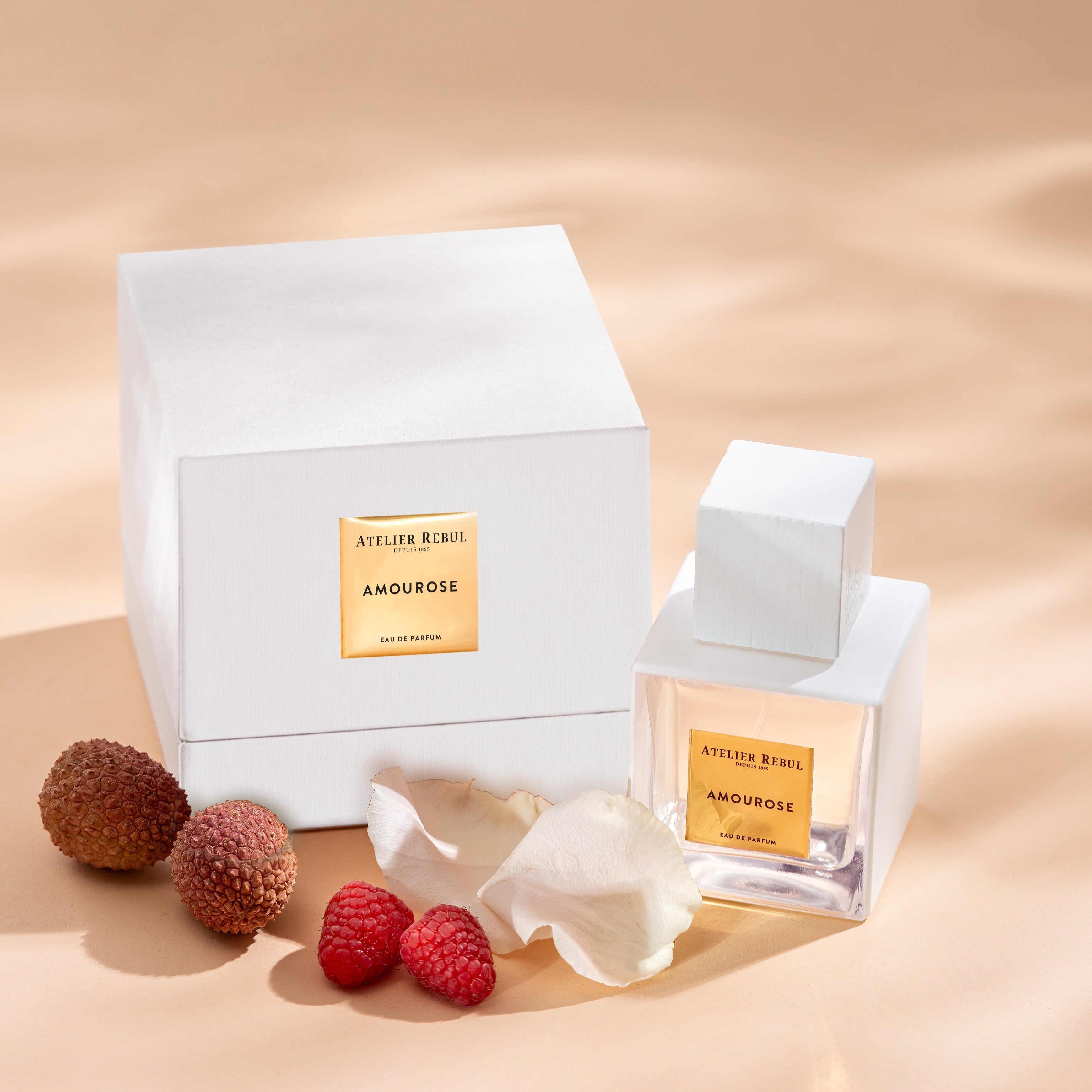 amourose parfumflasche in weissgold neben pruduktverpackung. fruechte im vordergrund.