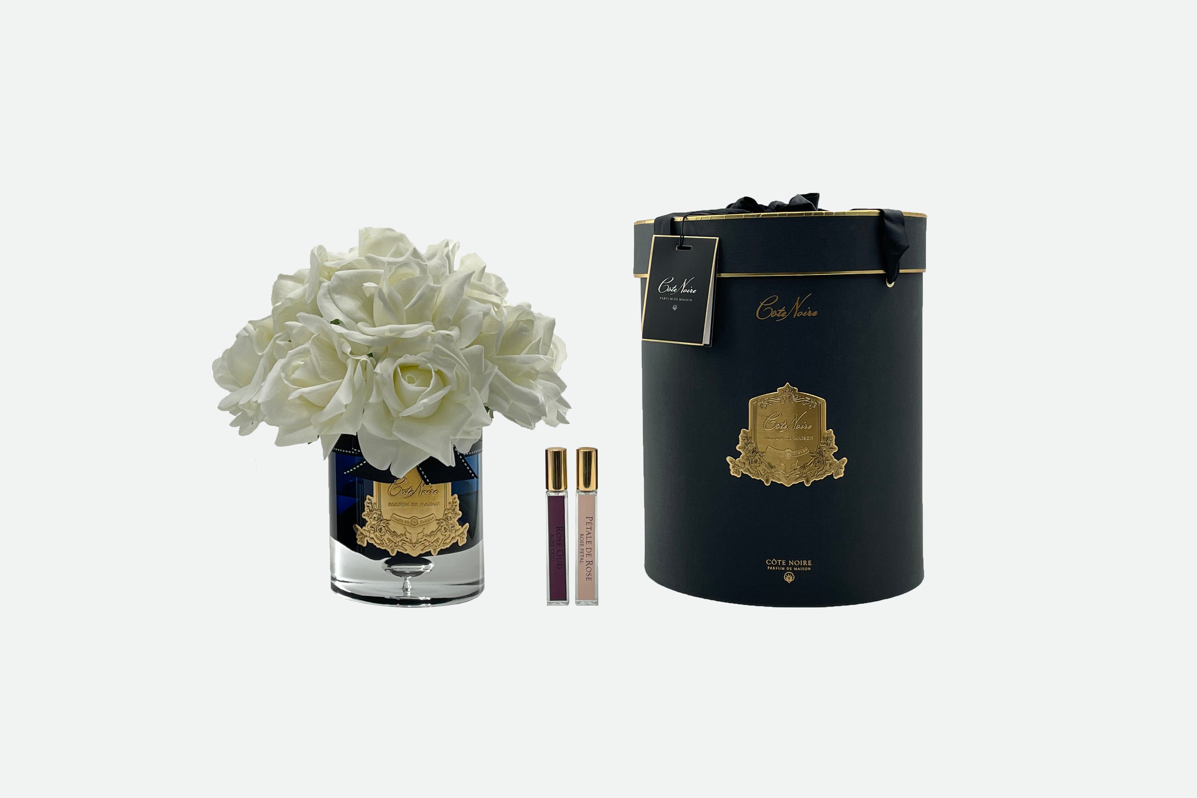 13 weisse rosen arrangiert in einer edlen glasvase, zwei parfumsprays und eine luxurioese runde dunkle geschenkbox.