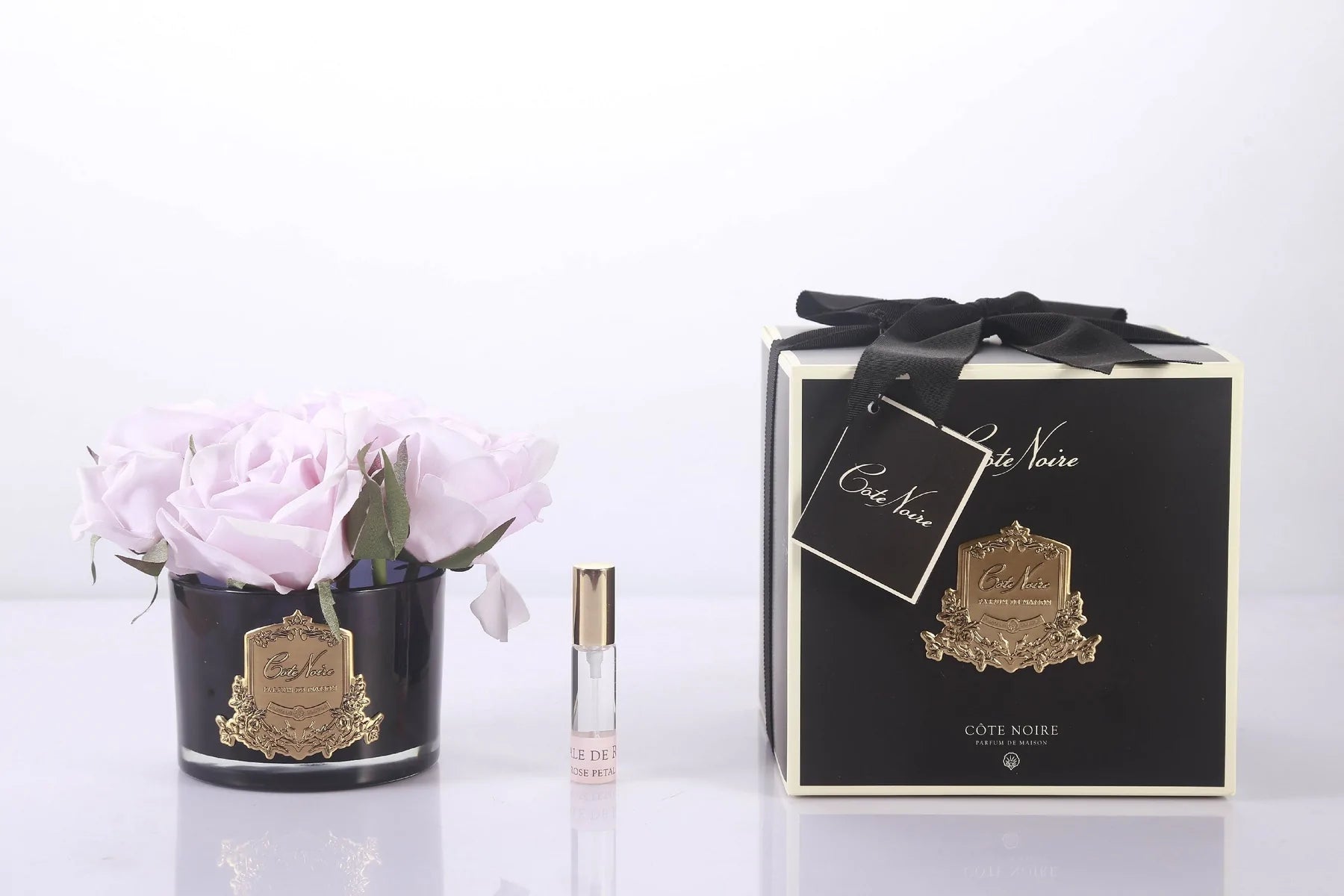 5 rosafarbene rosen in dunklem glas mit goldenem emblem. dazu duftspray und schwarze verpackung.