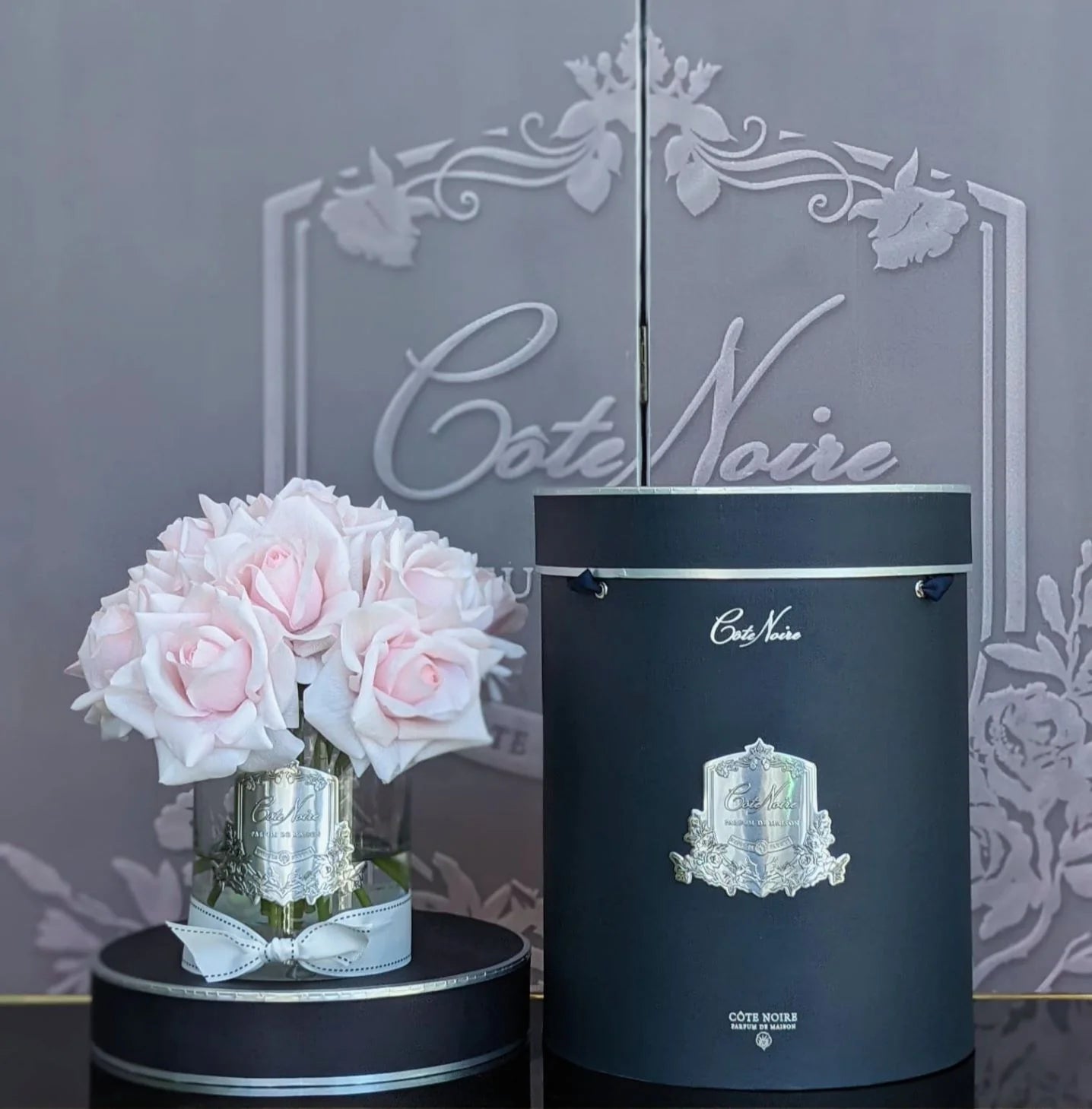 french pink rosen in hellem glas neben dunkler geschenkbox.