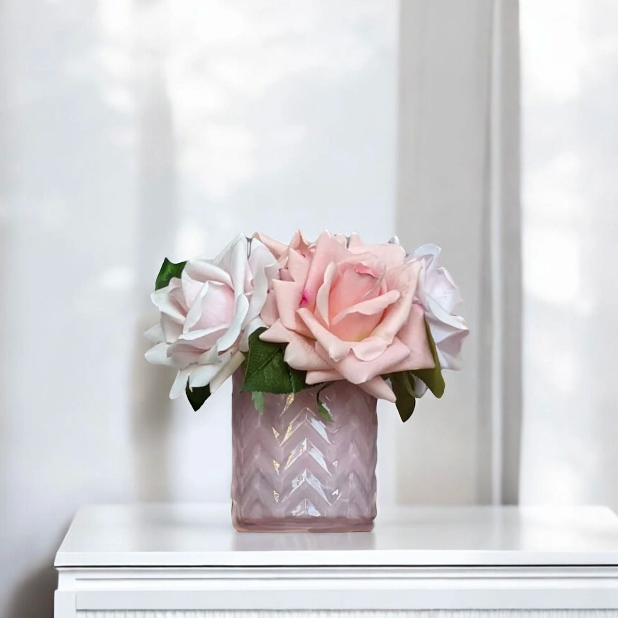 Kleines Arrangement aus pastellrosa und weißen Rosen in einem violetten Chevron-Vase auf weißem Hintergrund.