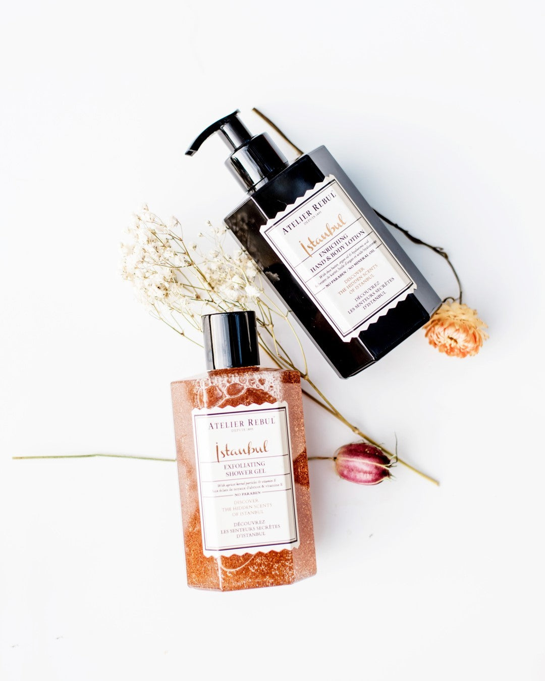 istanbul hand und bodylotion in schwarzer pumpflasche mit istanbul duschgel mit peeling auf weissem hintergrund mit blumen.