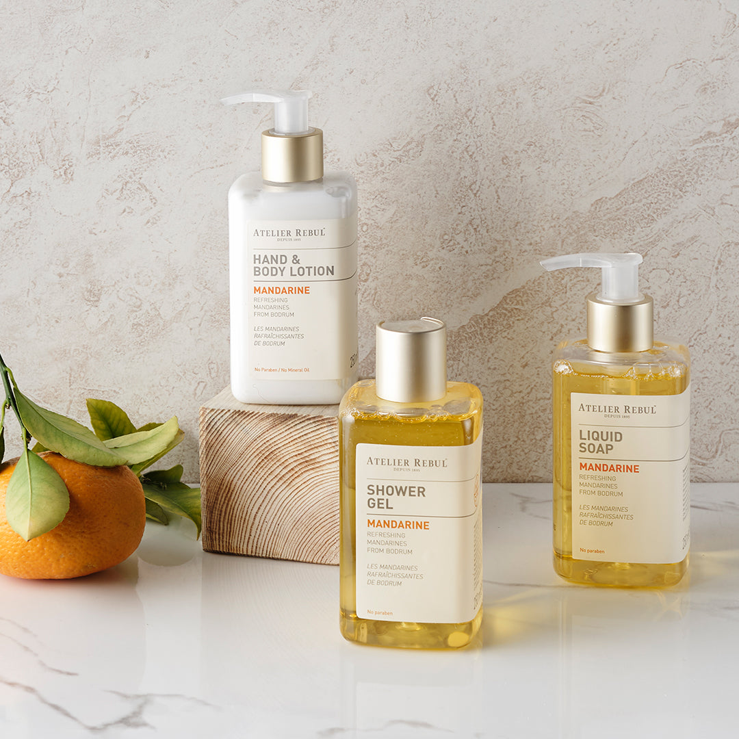 auf weissem marmor und einem holzklotz stehen 3 atelier rebul produkte und eine mandarine mit blaettern