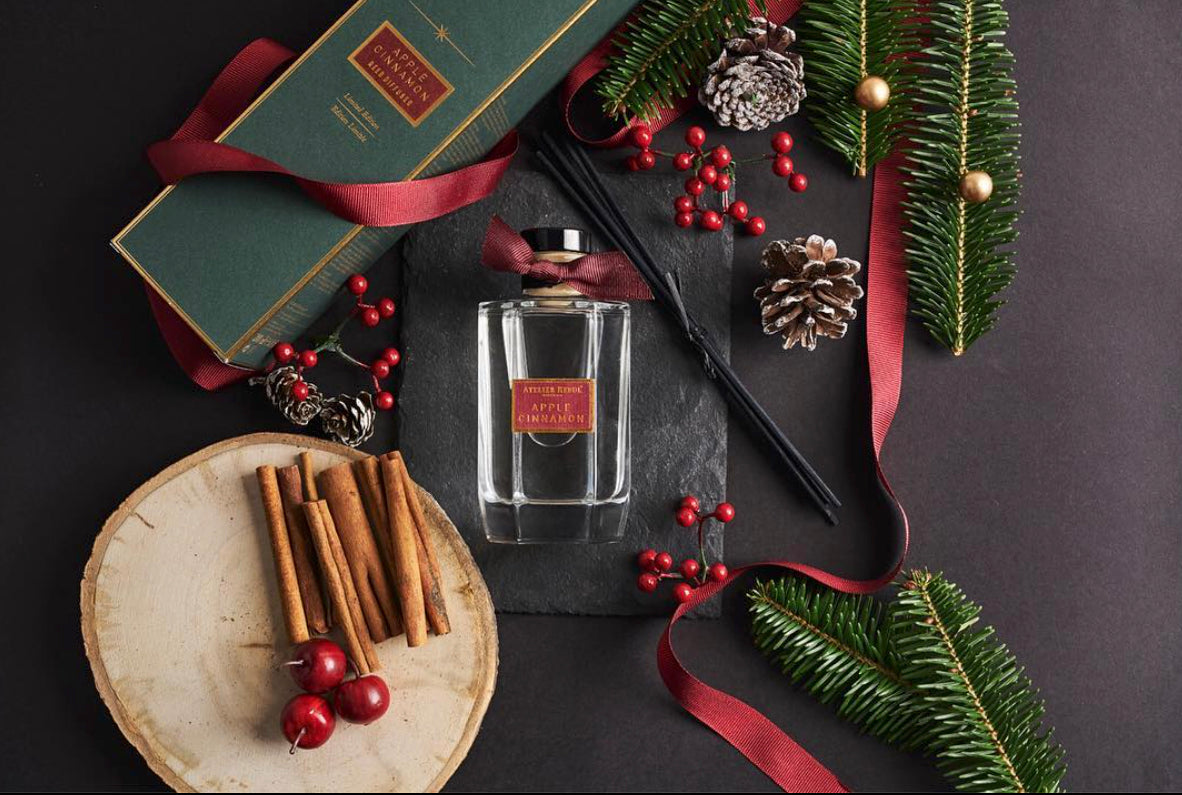 duftflasche, umgeben von tannenzweigen und -zapfen, roten beeren, sowie zimt und kirschen auf einem baumstamm.