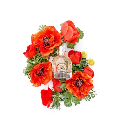 auf dem weissen hintergrund mit vielen mohnblueten liegt die glasspruehflasche edp schoene mohnblume