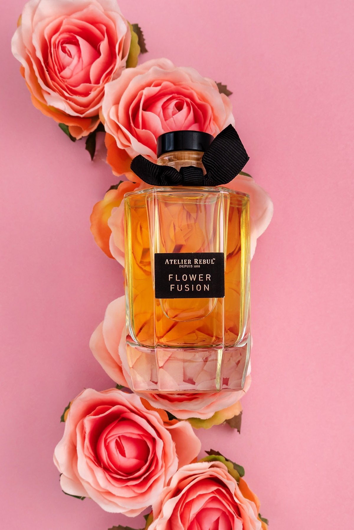 eine rosa rosenschlange liegt auf rosa hintergrund darauf die geschlossene atelier rebul flower fusion glasflasche