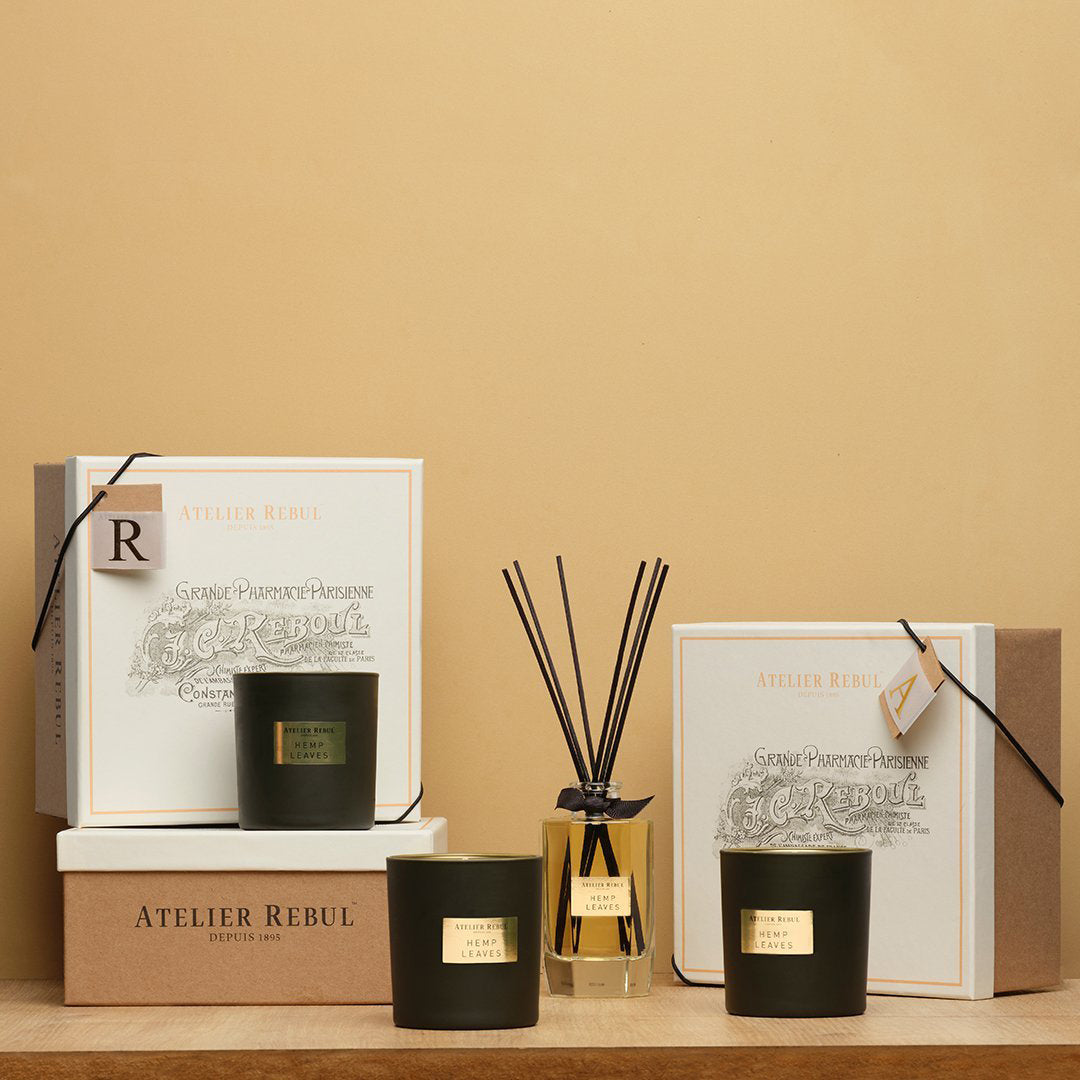 auf eine holzbrett vor beigem hintergrund stehen 3 geschenkboxen atelier rebul dazu dazugehörige duftkerzen und raumduft mit staebchen