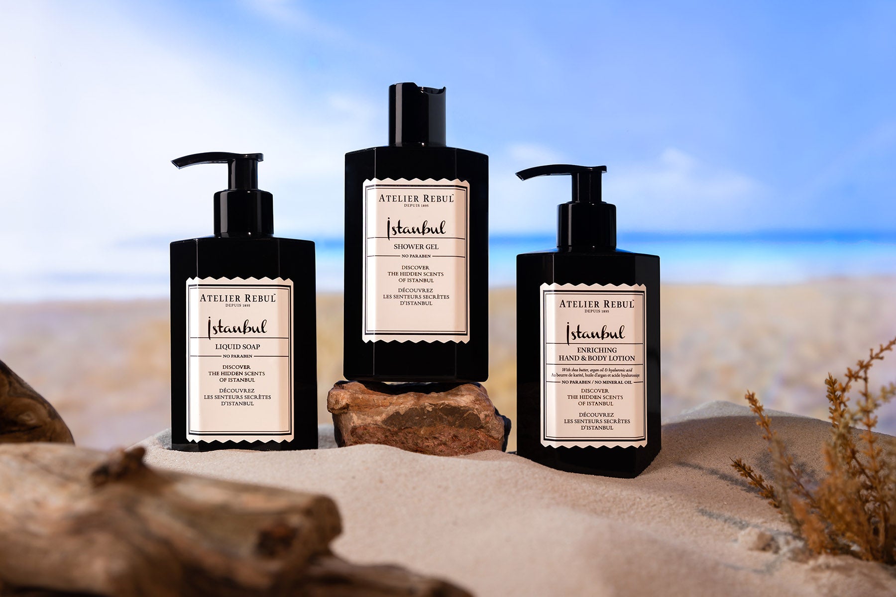 istanbul hand und bodylotion in schwarzer pumpflasche mit fluessigseife und duschgel auf sand und steinen