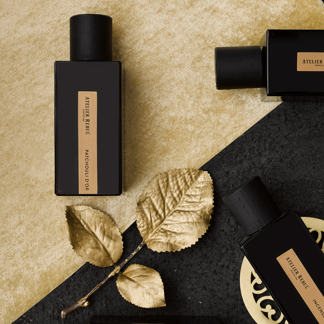 auf gold und schwarzem teppich liegen 3 schwarze mit goldenem etikett glasspruehflaschen dazu ein goldenes blatt
