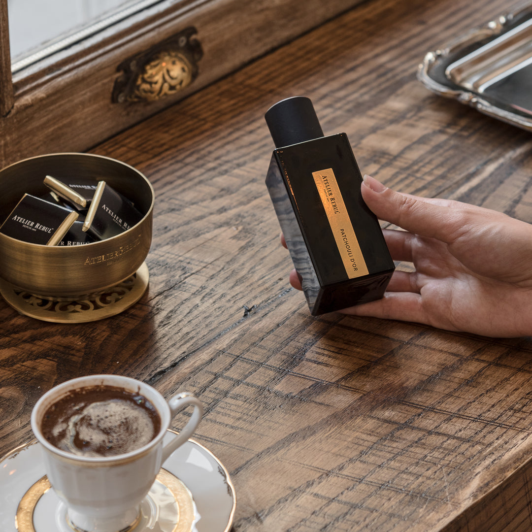 eine haltende hand liegt auf einem holztisch hier steht espresso und schokolade in der hand ist die atelier rebul flasche