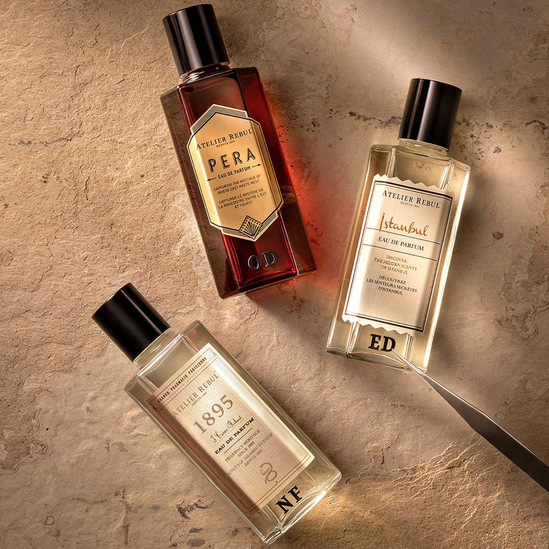 3 verschiedene eau de parfum von atelier rebul liegen auf einem hellen steinboden