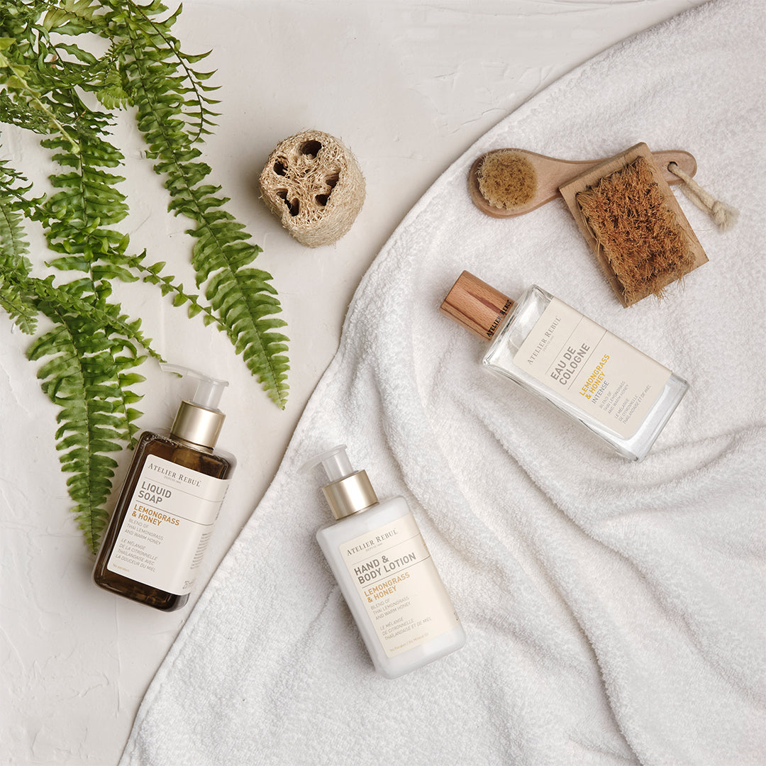 set aus seife, lotion und cologne auf einem weissen handtuch liegend neben gruener pflanze.