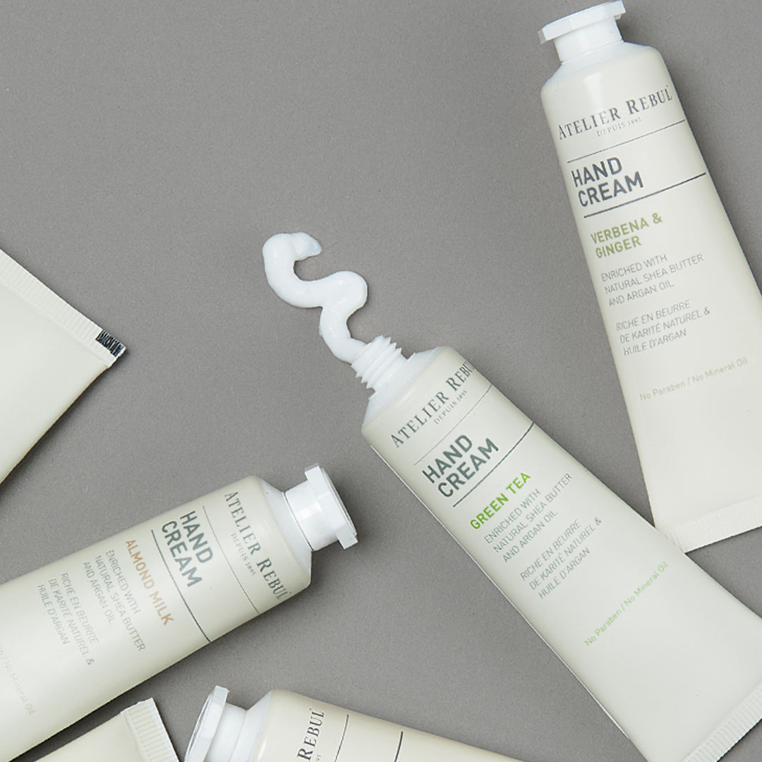 4 verschiedene kleine handcremes von atelier rebul liegen auf grauem hintergrund 1 davon ist geöffnet mit creme