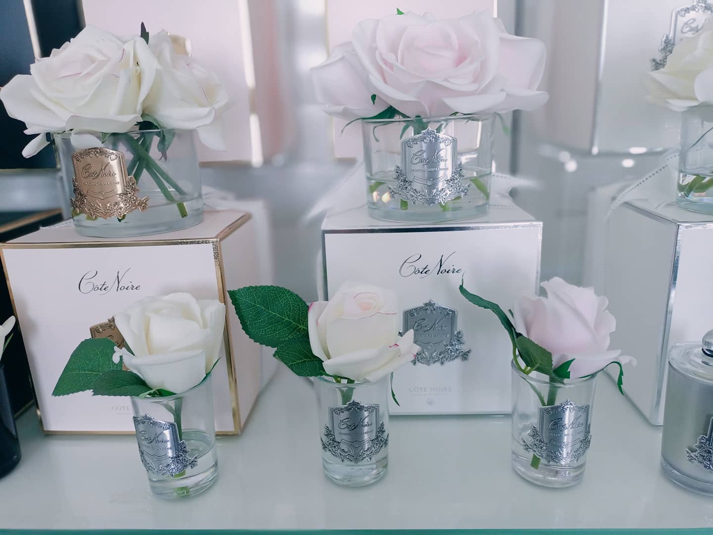 5 pinke duftblumen im glas auf produktverpackung. weitere duftrosen derselben reihe daneben.