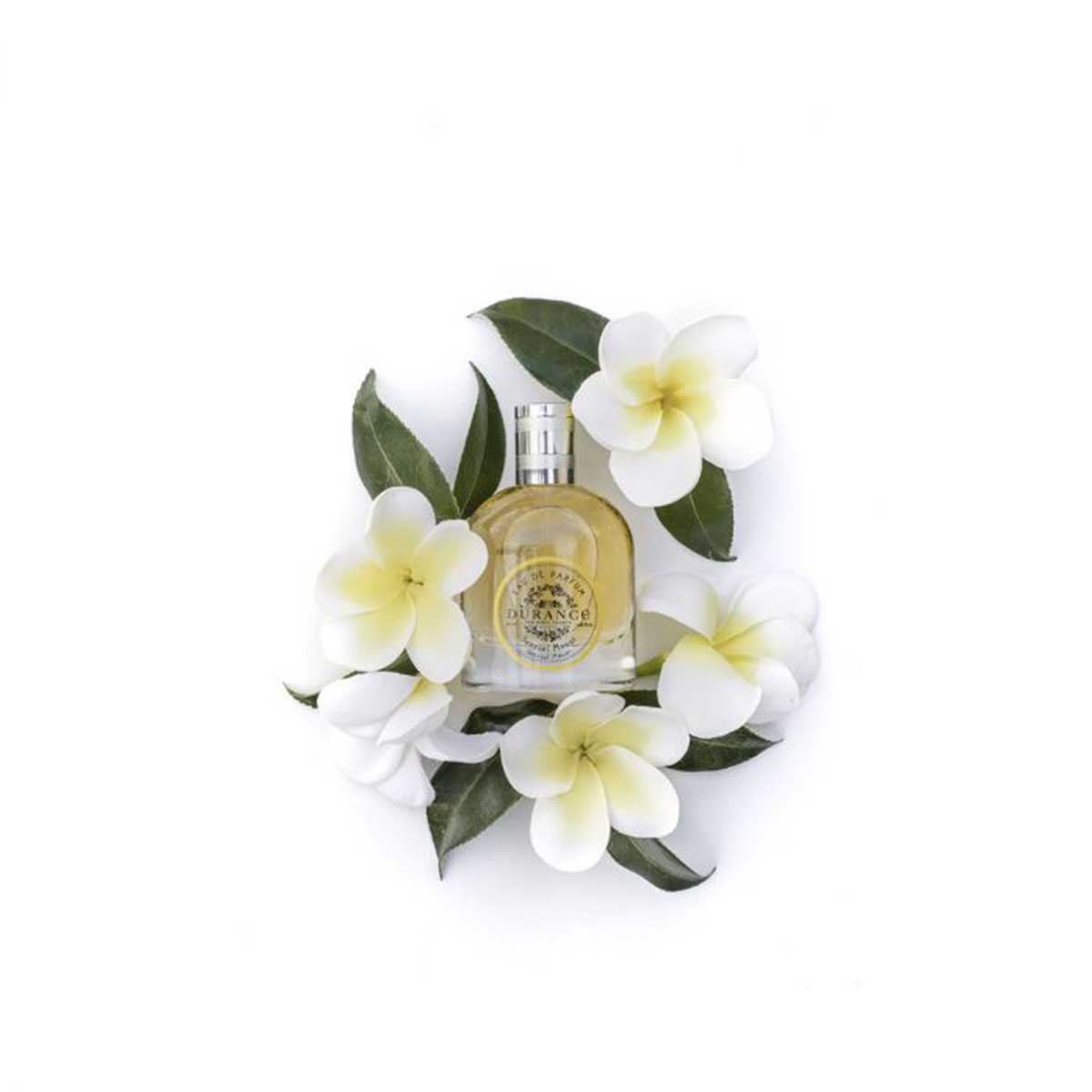 vor einem weissen hintergrund steht die edp flasche monoi die von weissen blumen umhuellt wird