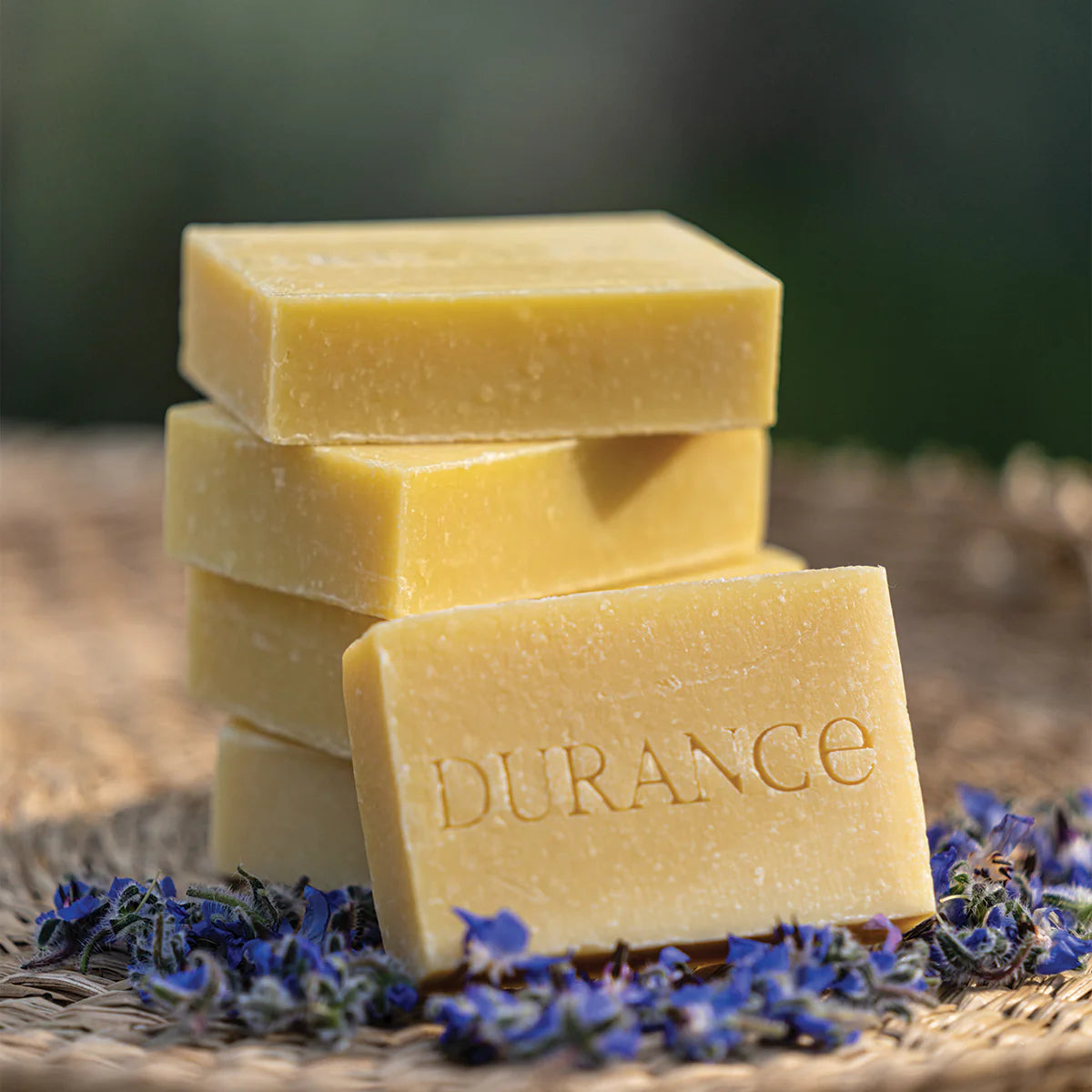 5 aufeinanderliegende  durance feste oelseifen auf einem weidenteller umhüllt von blueten