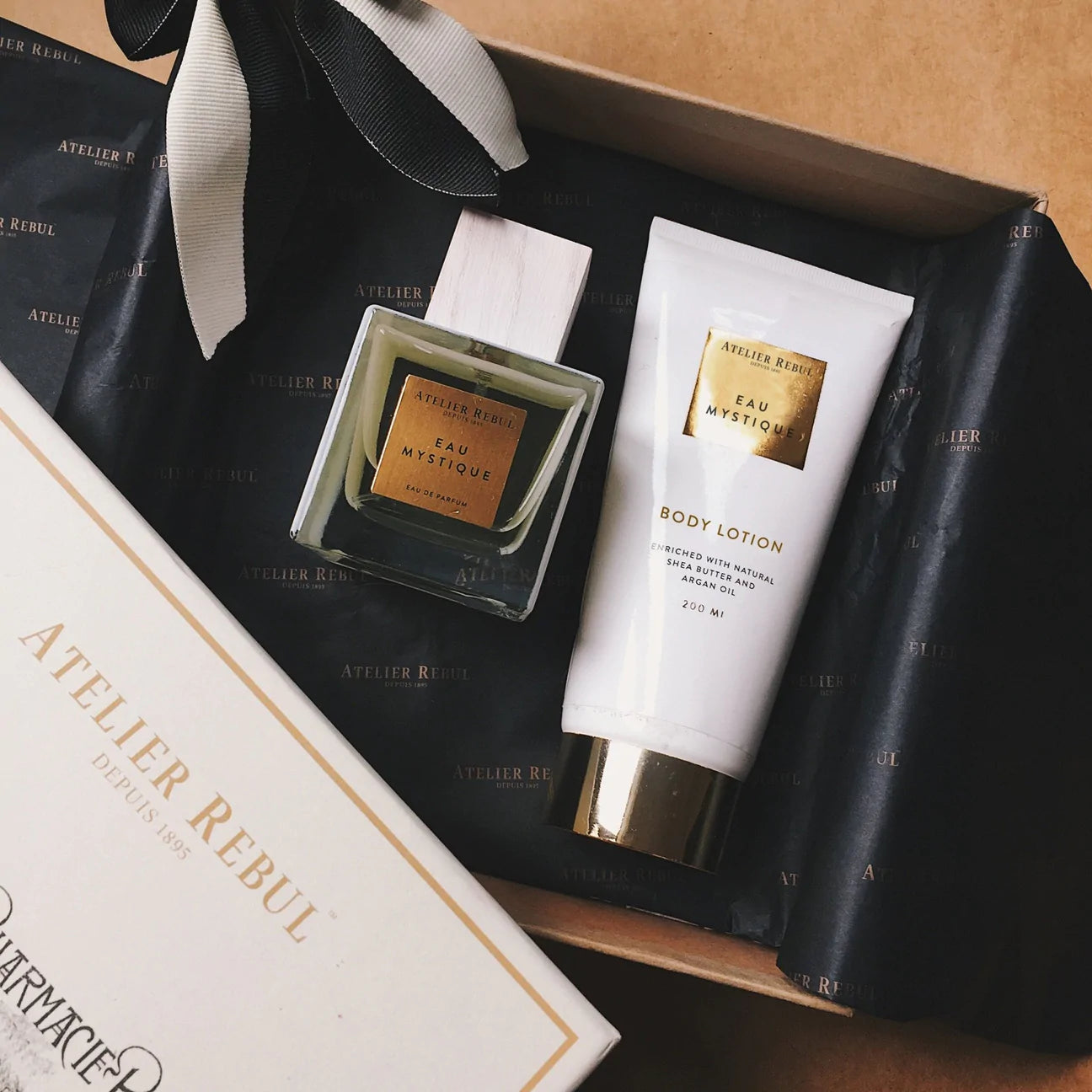 auf einem holztisch geschenkbox mit schwarzem seidenpapier darin bodylotion und eau de parfum