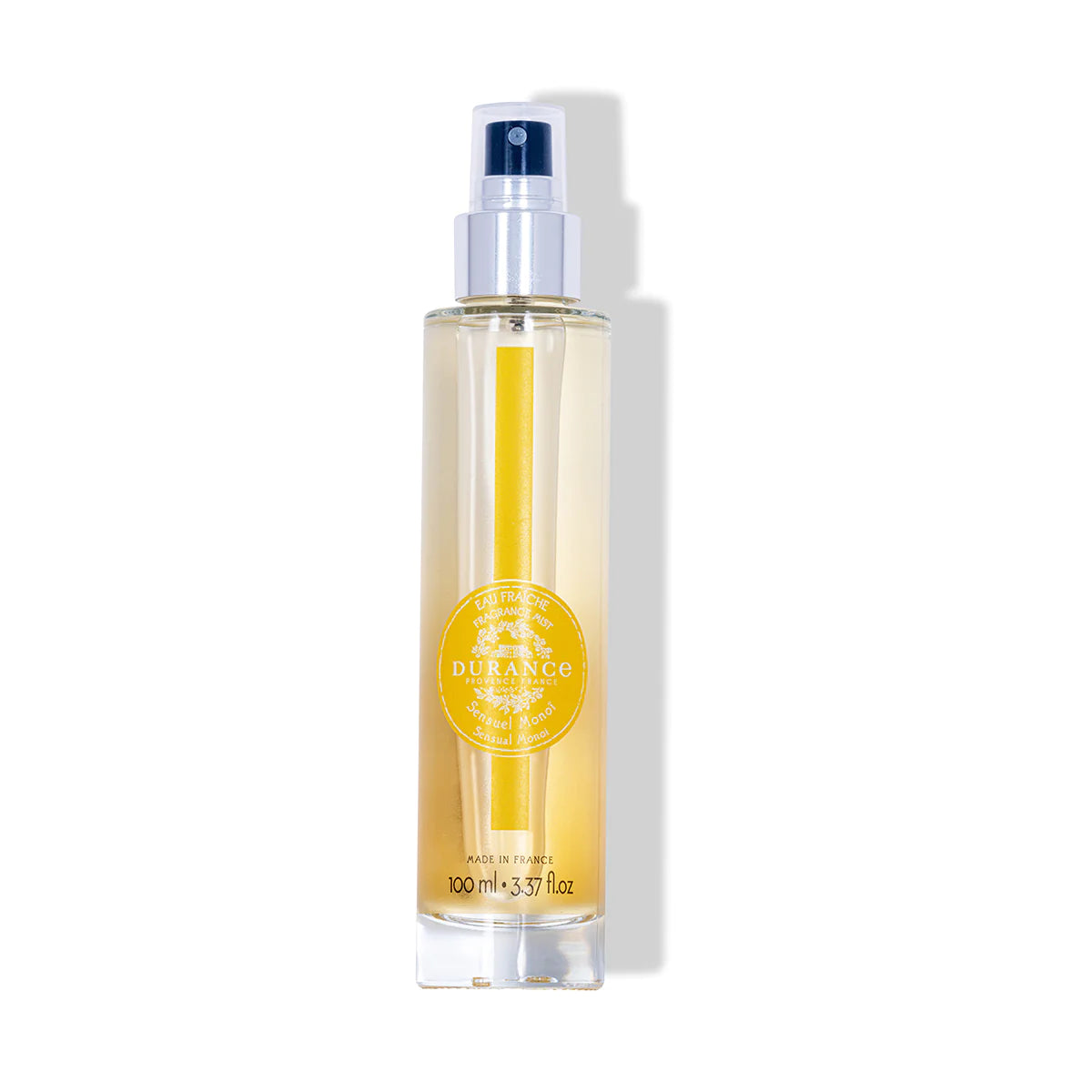 durchsichtige runde glasflasche eau fraiche sinnliches monoi mit silbernen spruehkopf vor weissem hintergrund