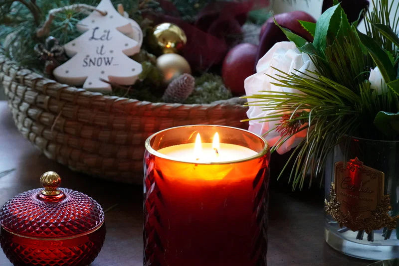 angezündete herringbone duftkerze vor einem holzkorb, der gefüllt ist mit tannenzweigen und lichtkugeln. weihnachtlich. let it snow.