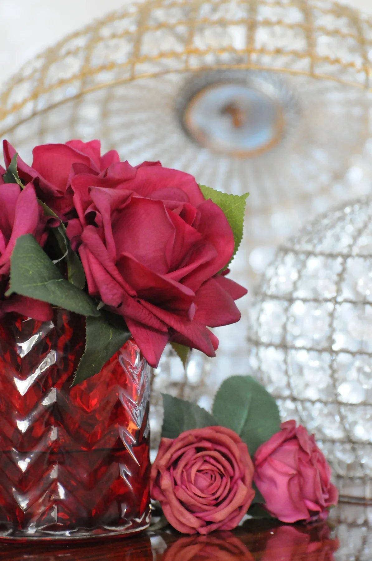 rote herringbone duftblume mit zwei roten rosen daneben liegend und kristalllampen im hintergrund.