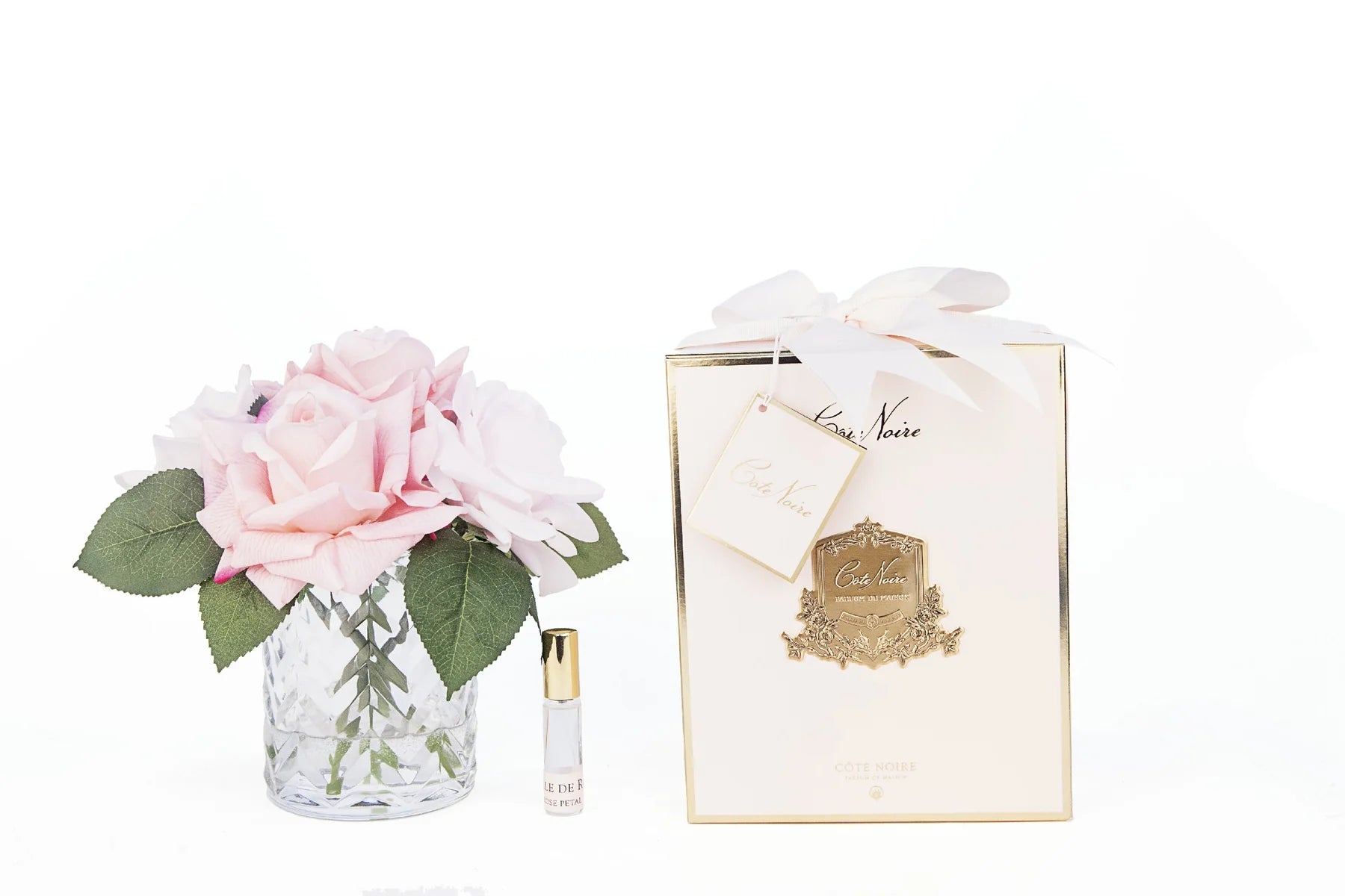 pinke rosen in durchsichtigem glas mit muster. daneben zwei parfumsprays und rosa geschenkbox mit schleife.
