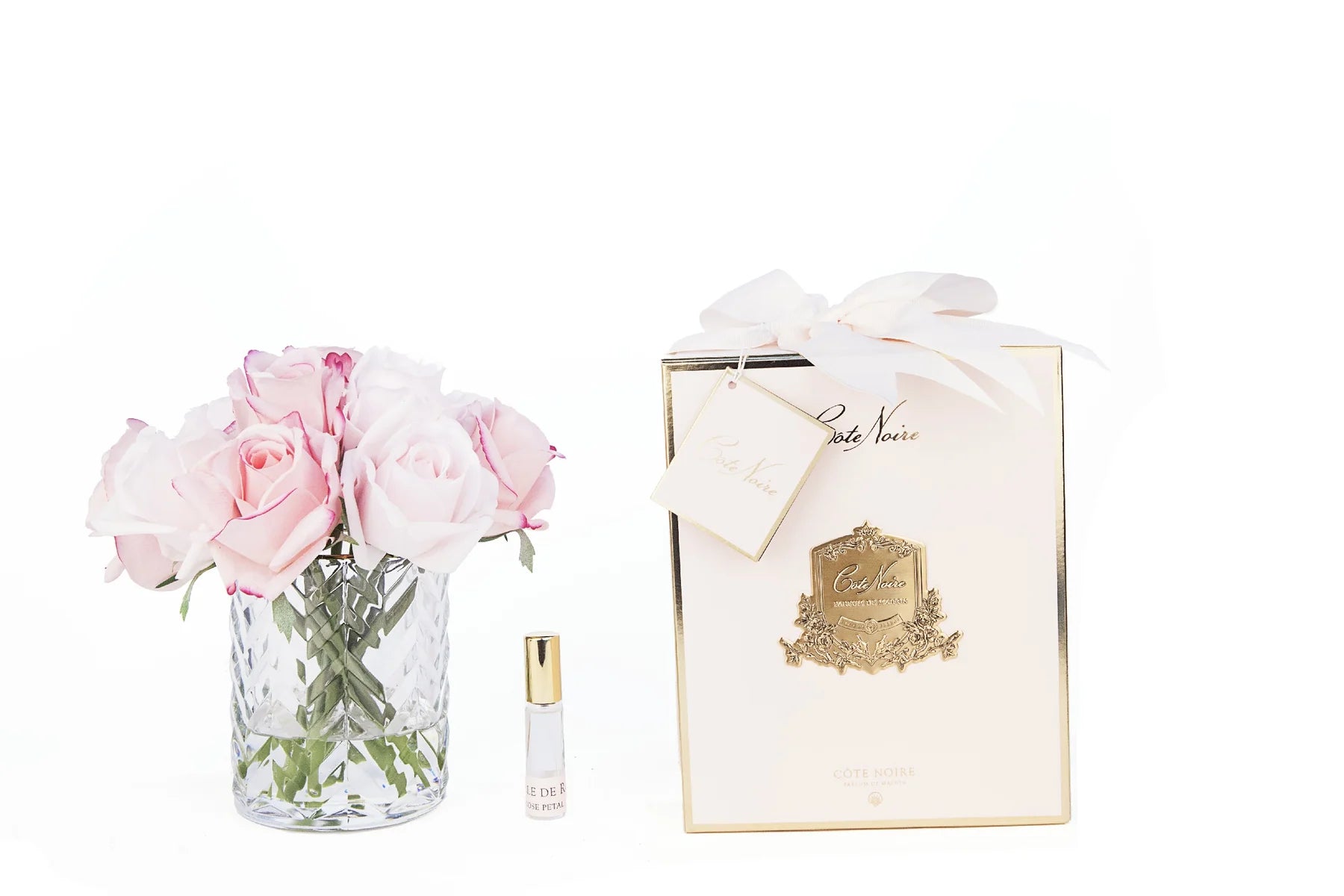 mixed pinke rosen in durchsichtigem glas mit muster. daneben zwei parfumsprays und rosa geschenkbox mit schleife.