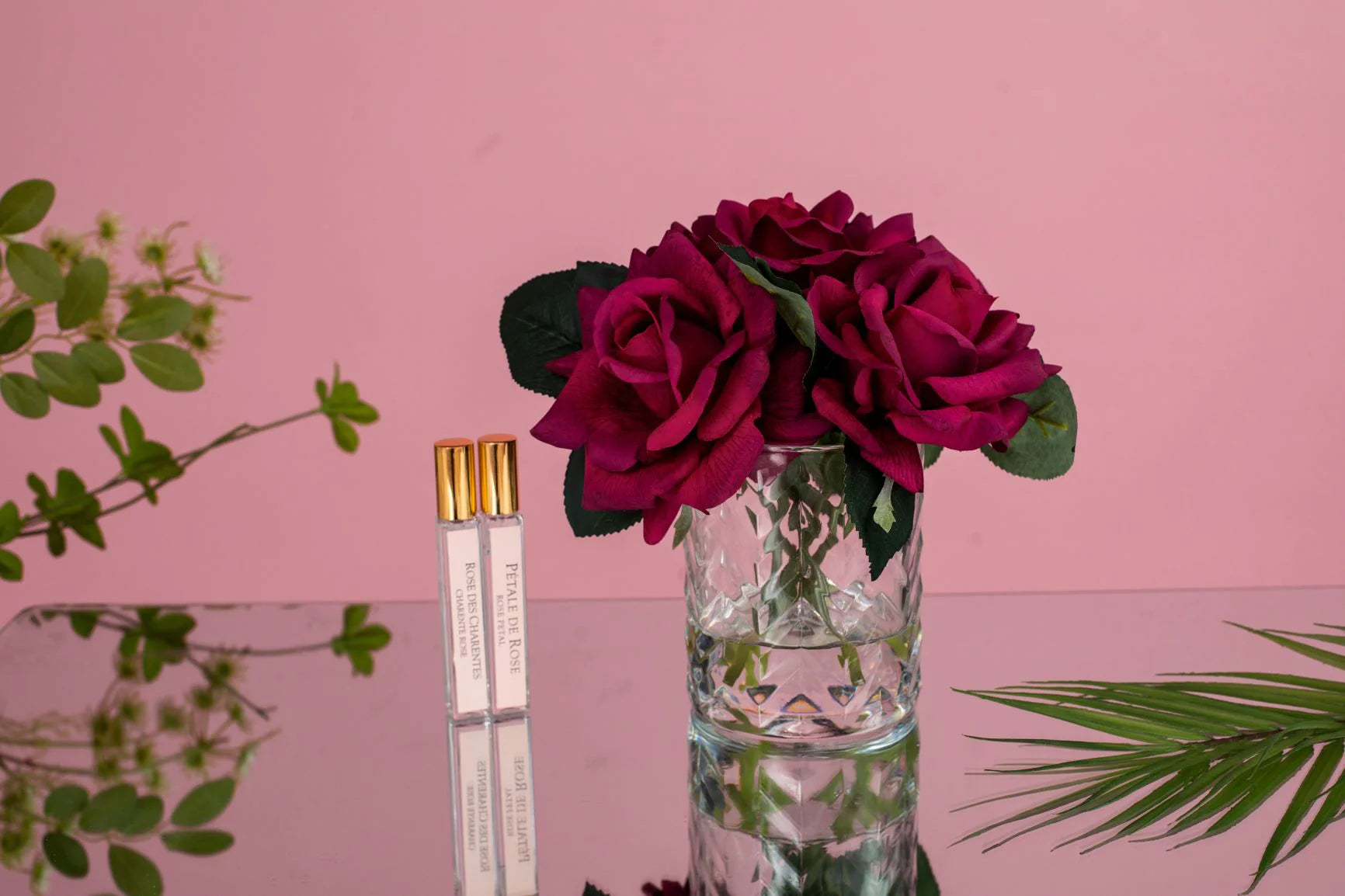 karminrote duftblumen im herringbone auf glastisch, der den rosa hintergrund spiegelt.