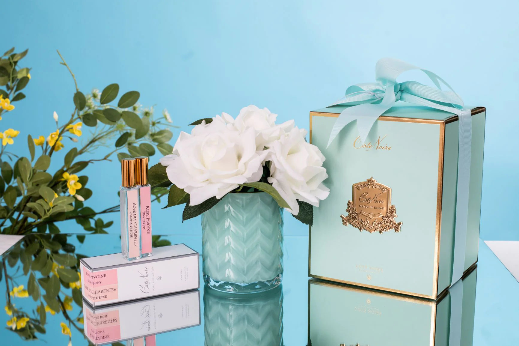 set aus zwei parfumsprays, weisser herringbone duftblume mit blauer vase und blauer geschenkbox mit schleife.