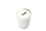 herringbone duftkerze vor weißem hintergrund. fokus auf luxuriösem golddeckel mit feiner skulptur einer lilie.