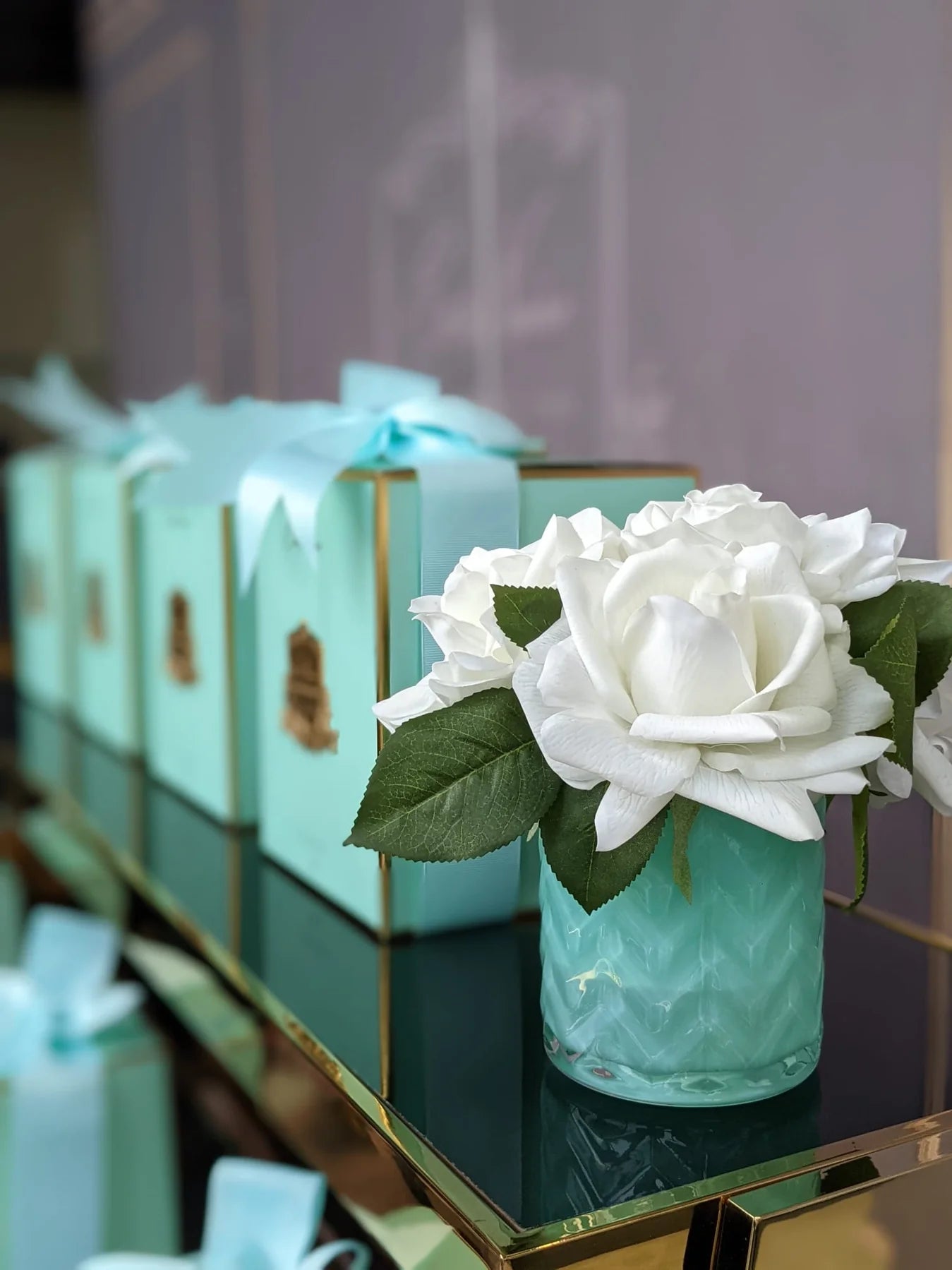 seitenansicht der jade duftblume neben einer reihe blauer verpackungsboxen mit schleife.