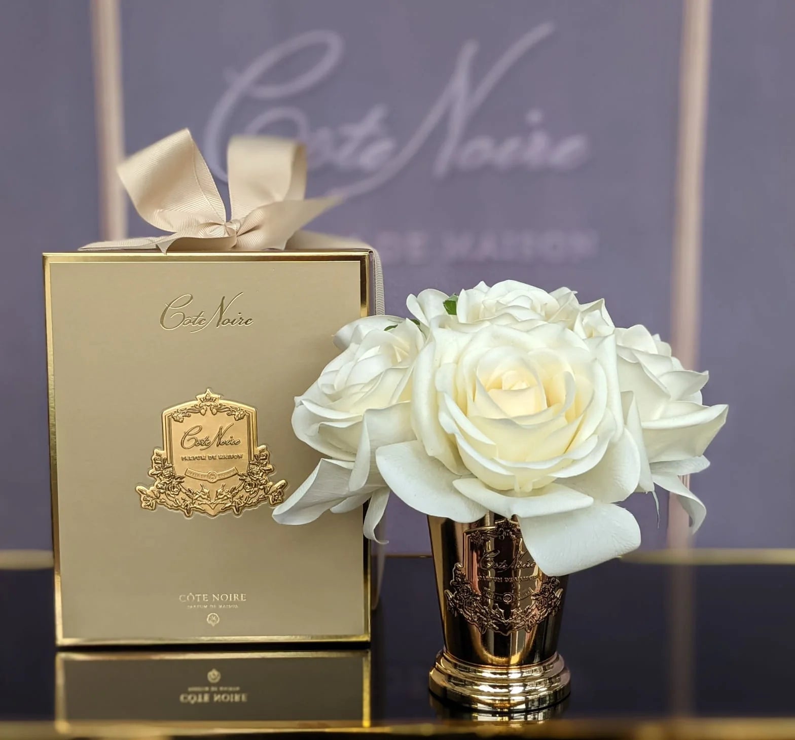 sieben rosen duftblume in goldenem kelch neben geschenkbox auf gold blauem praesentiertisch.
