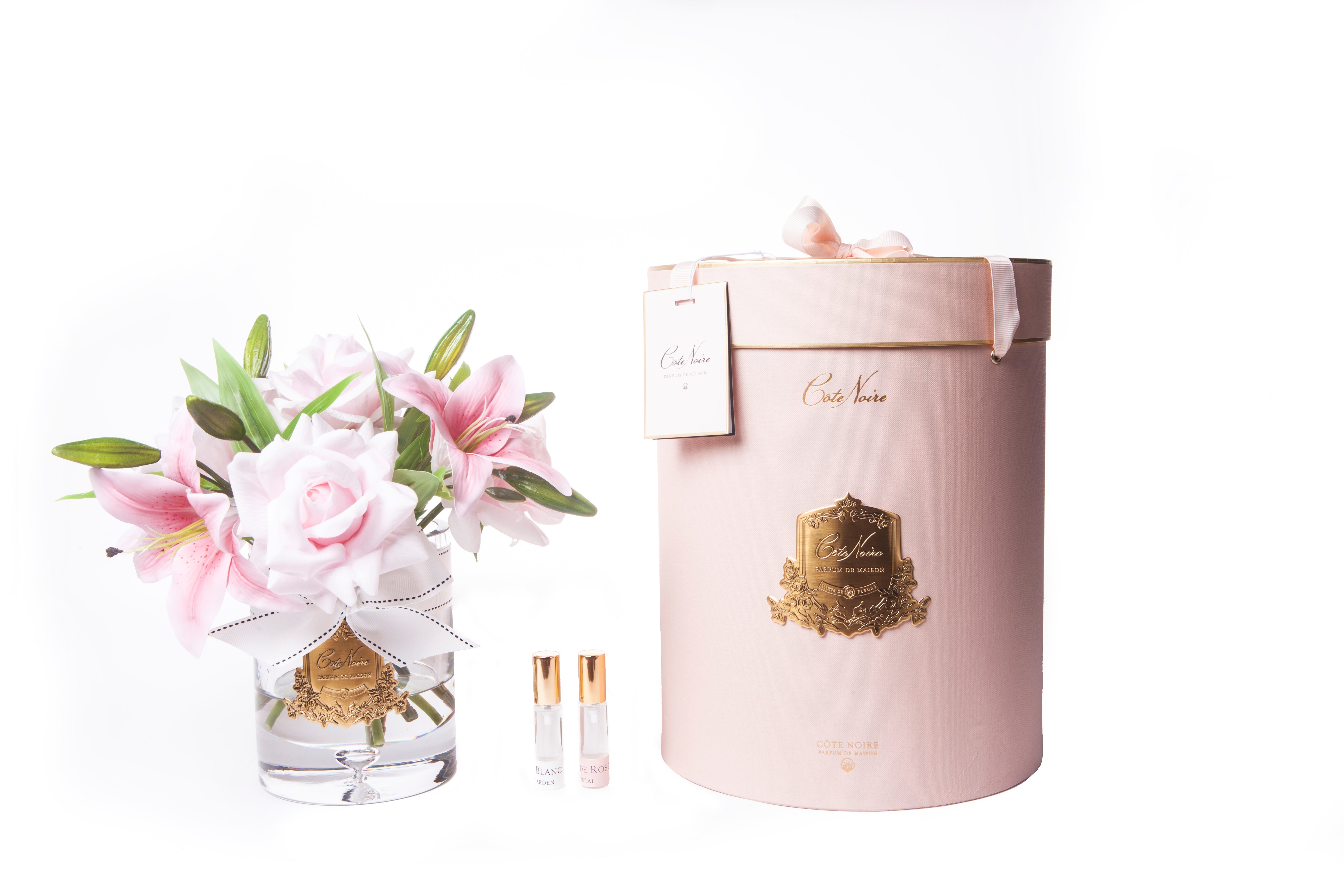 pinke luxury lilies duftrosen im glas neben pinker zylenderbox. dazwischen zwei parfumsprays.