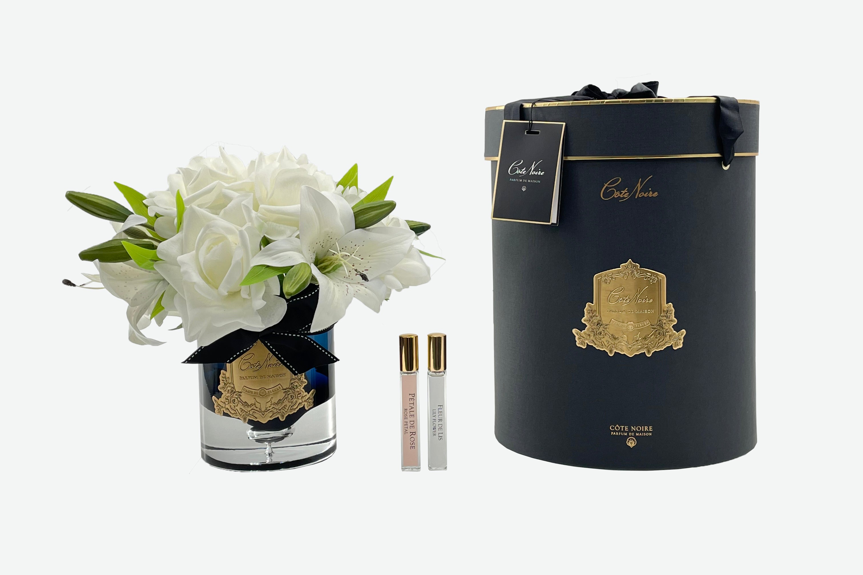 weisse luxury lilies duftrosen im glas neben schwarzer zylenderbox. dazwischen zwei parfumsprays. weisser hintergrund.