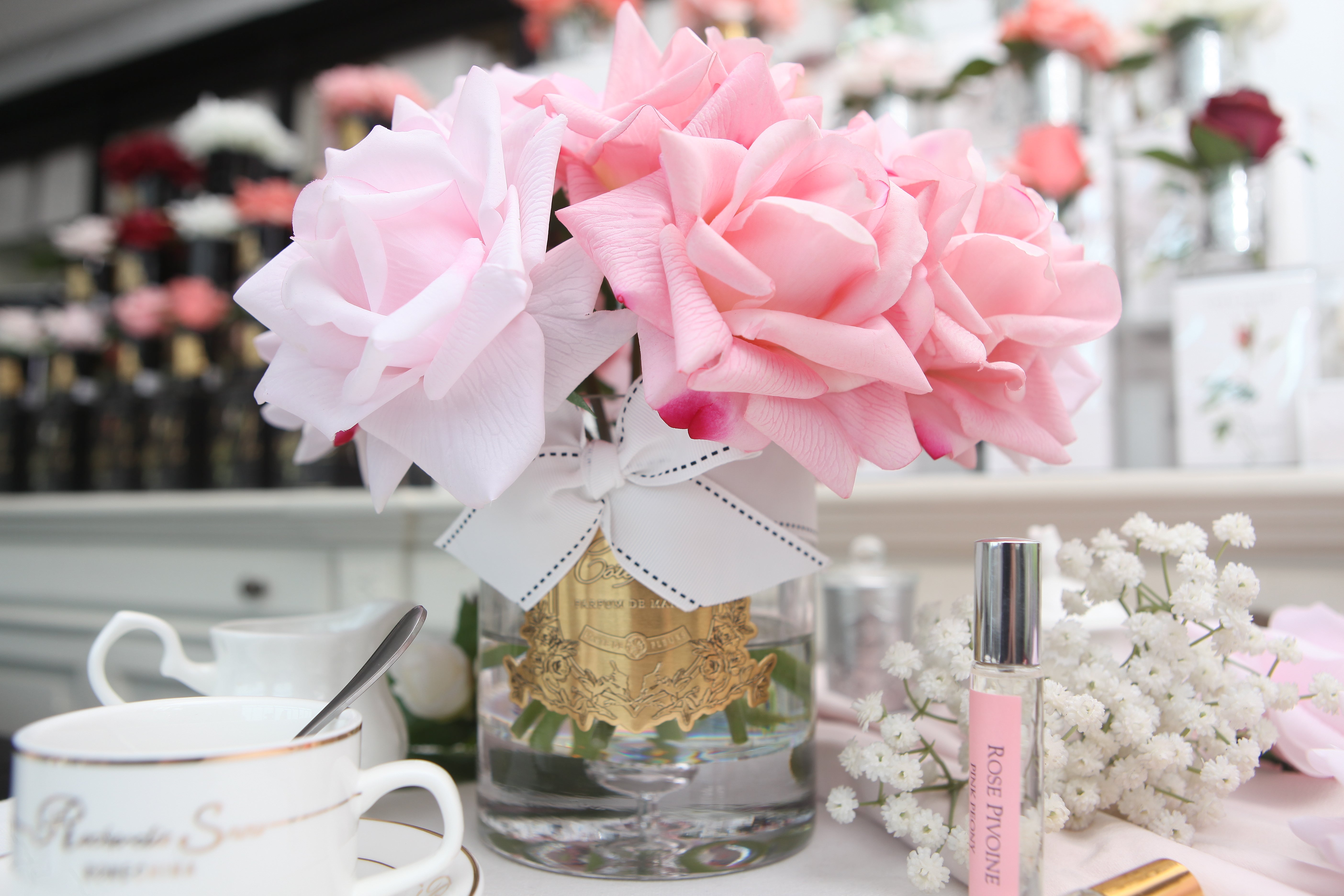 mixed pink rosen in hellem glas mit goldener inschrift und weisser schleife auf gedecktem tisch. helle farben