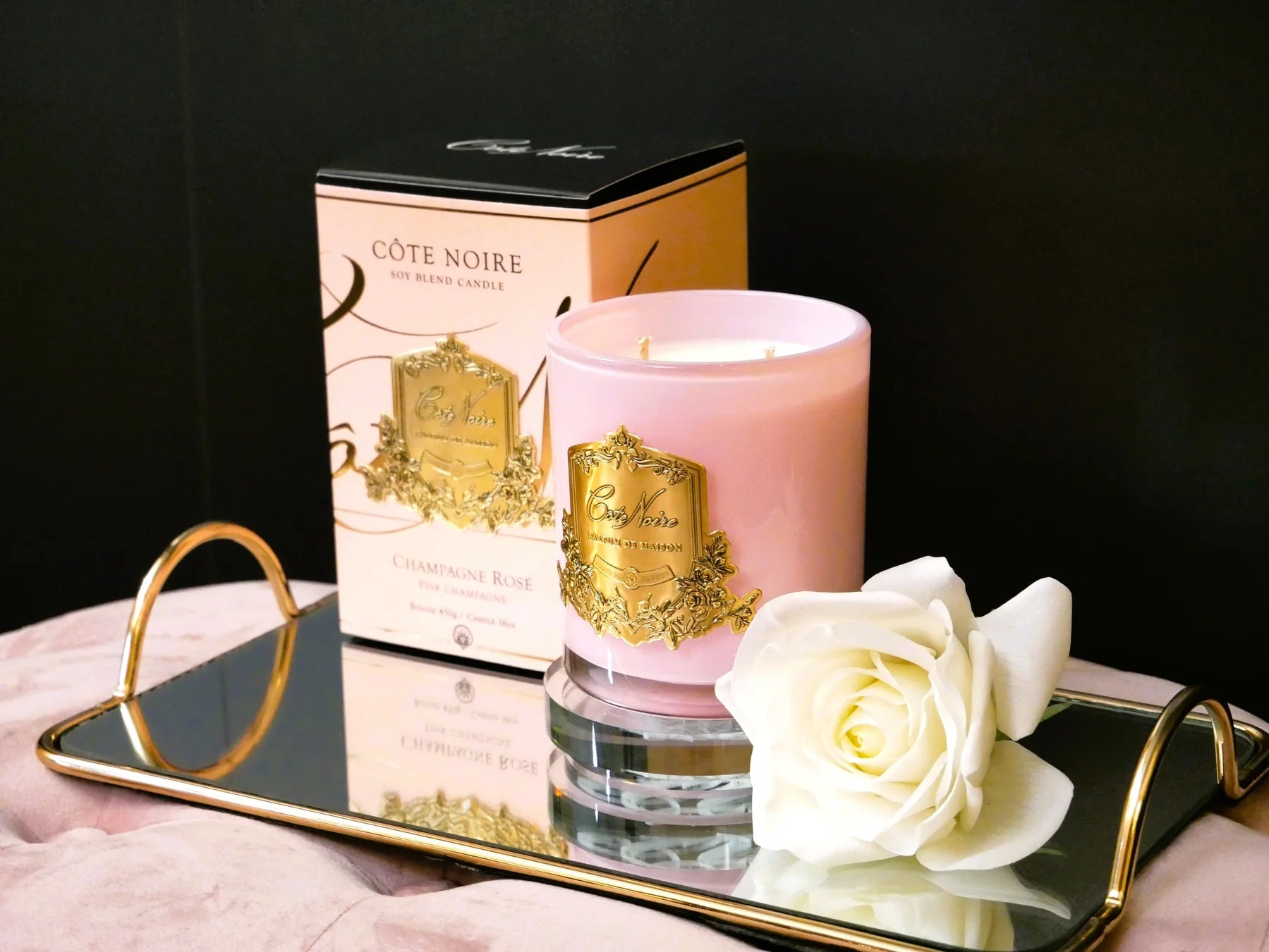 pinke duftkerze mit goldener inschrift, pinke verpackung und weisse single rose auf goldenem serviertablett. seitenansicht.