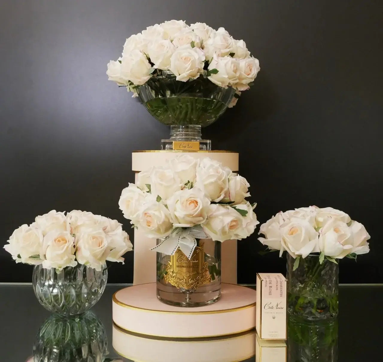 Blush Duftrosen in verschiedenen Glasvasen mit Côte Noire Parfum – elegantes Arrangement auf runden Boxen in zarten Rosétönen