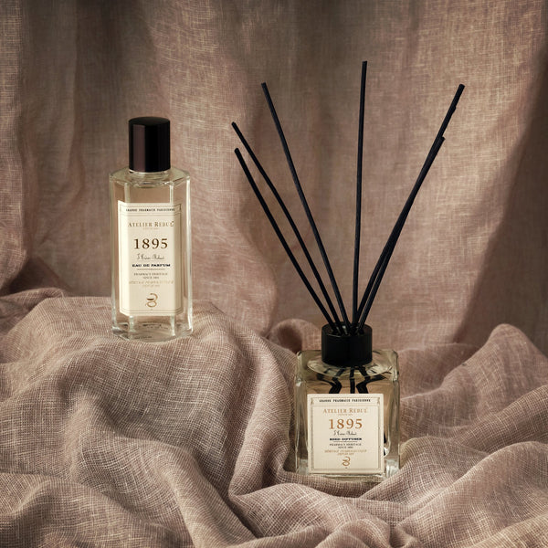 1895 duftstaebchen und eau de parfum auf einem dezenten beigen leinentuch.