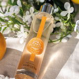 liegende durchsichtige glasspruehflasche eau fraiche baumwoll moschus auf einem weissen tisch mit blueten