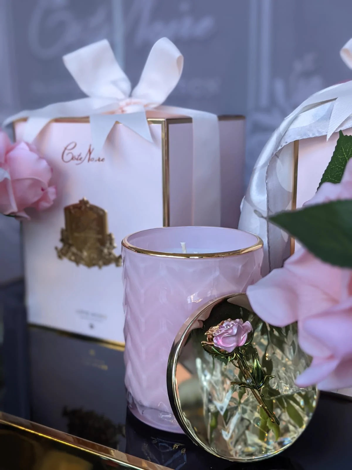 rosa herringbone duftkerze und geschenkbox auf blauem glastisch. golddeckel für besseren blick auf rose angelehnt.