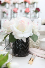 5 weisse duftblumen mit pinkem rand in schwarzem, gemustertem glas auf esstisch. daneben liegendes duftspray.
