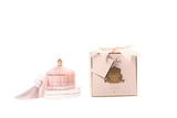cote noire art duftkerze in dekorativem glas mit quaste, daneben verpackung mit geschenkschleife, pink und gold.