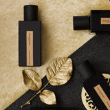 auf gold und schwarzem teppich liegen 3 schwarze mit goldenem etikett glasspruehflaschen dazu ein goldenes blatt