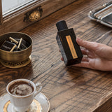 eine haltende hand liegt auf einem holztisch hier steht espresso und schokolade in der hand ist die atelier rebul flasche