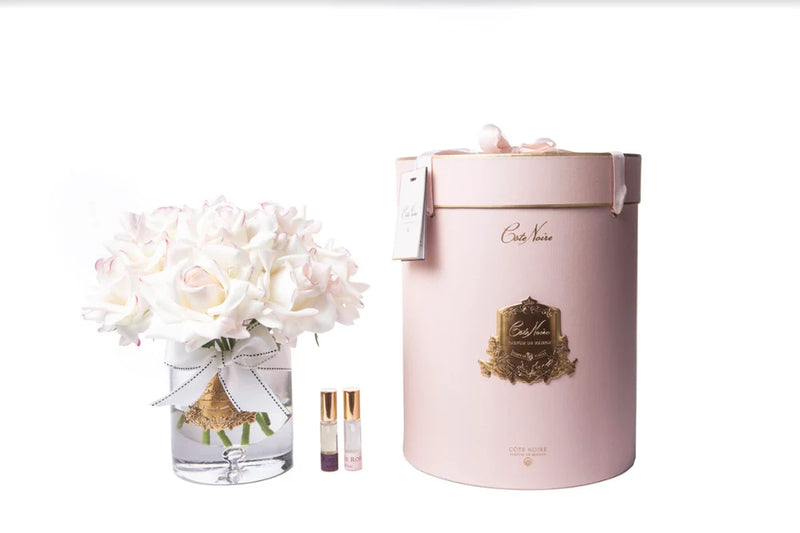 13 weiße rosen mit pinken enden in einer edlen glasvase, zwei parfumsprays, eine luxurioese runde geschenkbox in rosa.